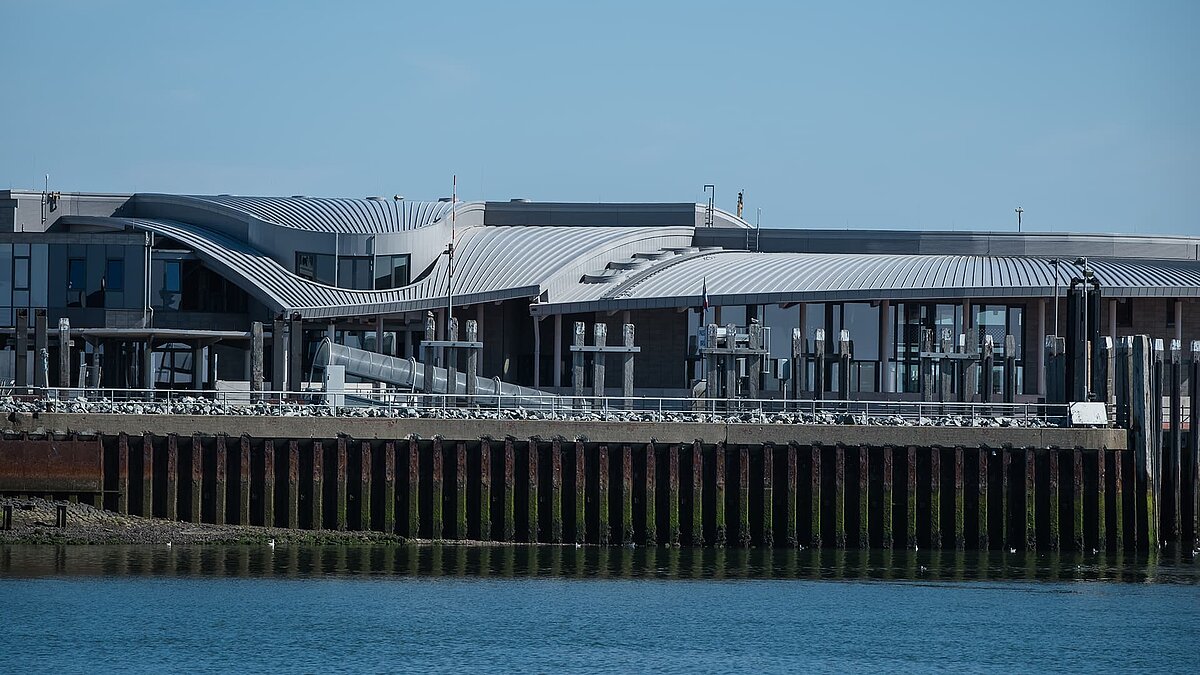 Hafenterminal Norderney mit modernem, wellenförmigem Dach und Glasfassaden am Wasser.