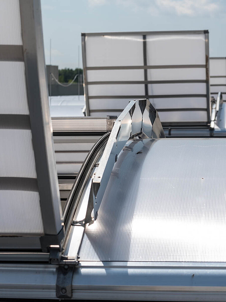 Geöffnetes LAMILUX Lichtband B RWA mit bogenförmiger Verglasung und sichtbarer Antriebstechnik auf Flachdach
