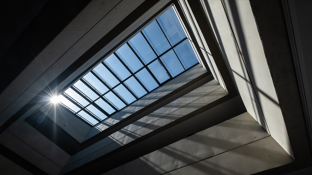 Blick auf das Glasdach der Bertha-von-Suttner-Realschule in Köln, mit einfallendem Sonnenlicht und Schatteneffekten.