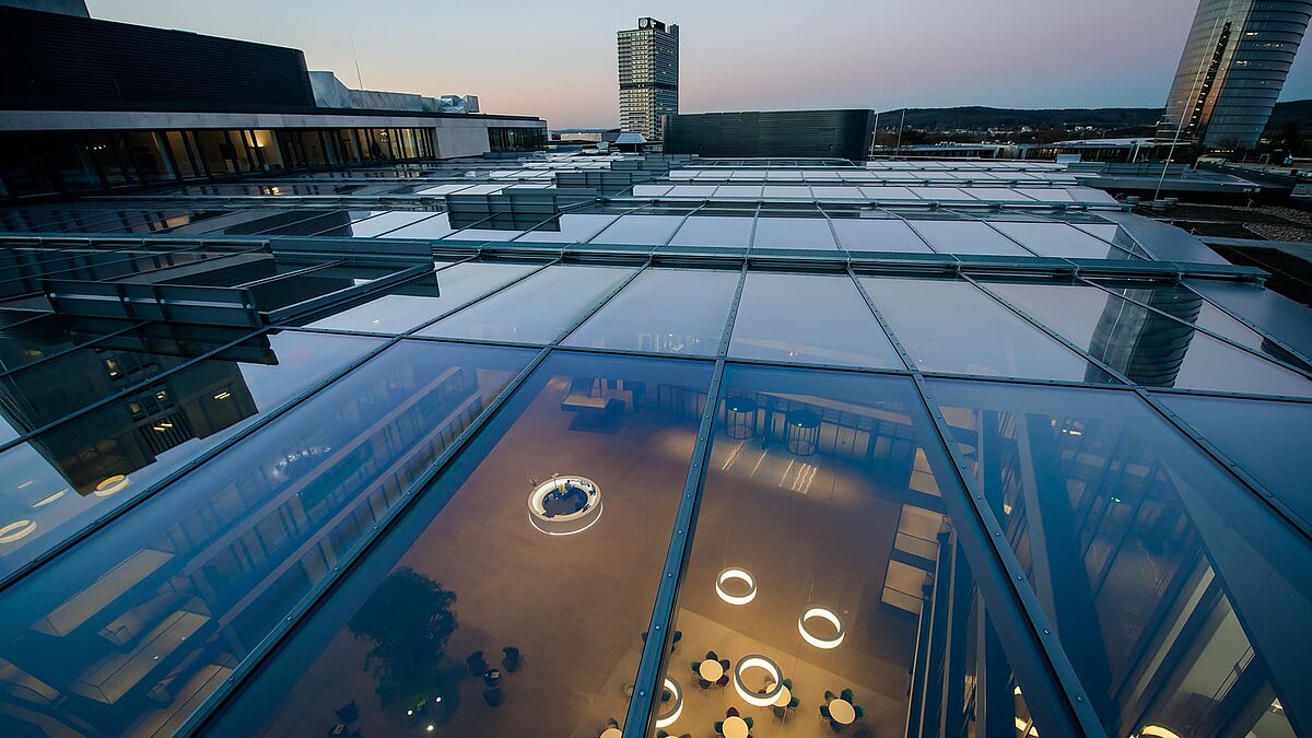 Glasdach des FGS Campus bei Dämmerung, das den Innenbereich mit modernen Leuchten und Möbeln zeigt.