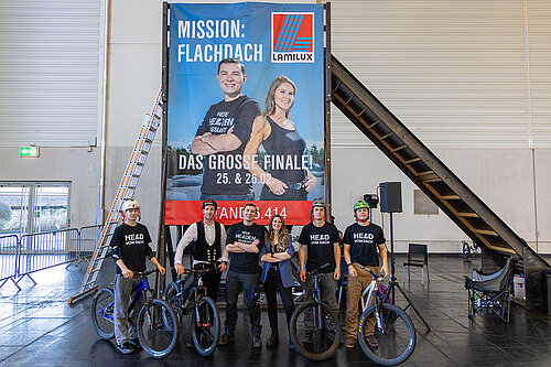 LAMILUX Mission Flachdach Finalisten mit Fahrrädern vor Event-Banner auf Fachmesse