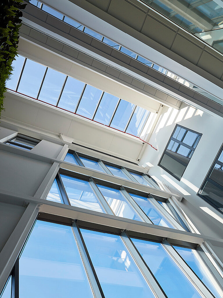 Innenansicht eines mehrgeschossigen Gebäuderaums mit großflächiger Verglasung, Galerieebenen und einfallendem Tageslicht von oben