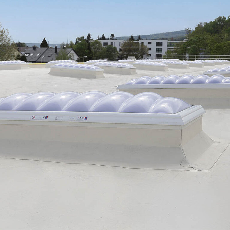 Mehrere LAMILUX Lichtkuppeln F100 W auf weißem Flachdach zur großflächigen Tageslichtversorgung
