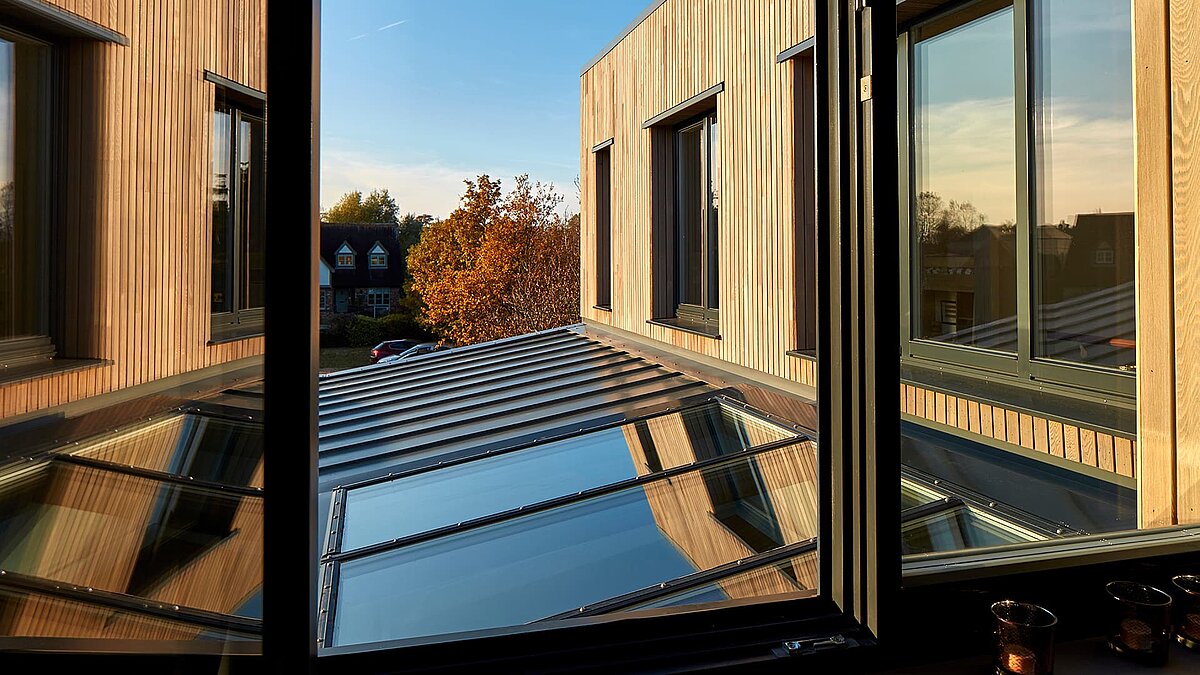 Blick aus einem Fenster auf das Glasdach und die Fassade des Potton Show Homes in England bei warmem Sonnenlicht.
