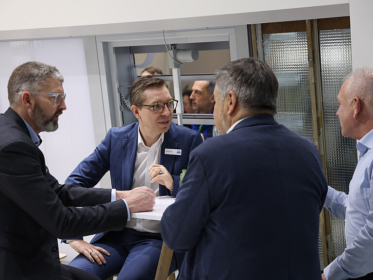 Gruppe von vier erwachsenen Männern in einem beruflichen Gespräch, sitzend in einem modernen Innenraum und diskutieren