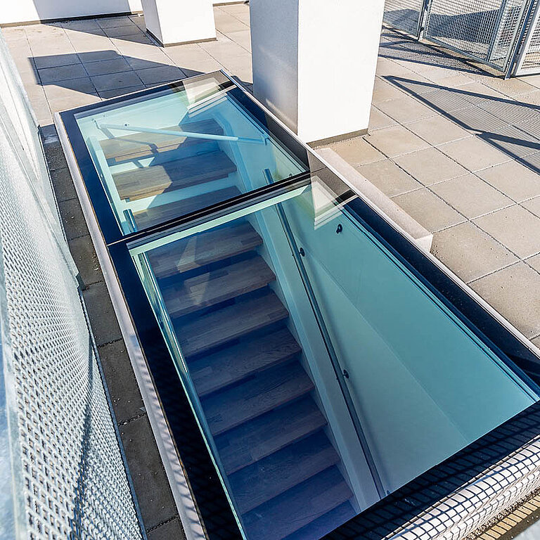 Geöffneter LAMILUX Flachdach Ausstieg mit transparenter Verglasung und integrierter Treppe für sicheren Dachzugang