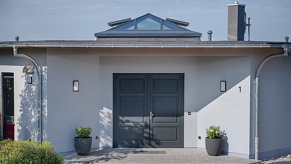 Moderne Eingangsfassade eines Einfamilienhauses in Wichmannsdorf mit dunkelgrauer Doppeltür und Glaspyramide auf dem Dach.