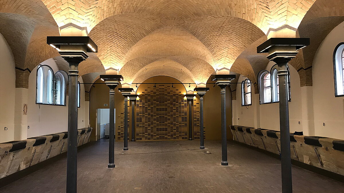 Historischer Innenraum der Leibniz-Universität Hannover mit Backsteingewölbe, gusseisernen Säulen und Bogenfenstern.