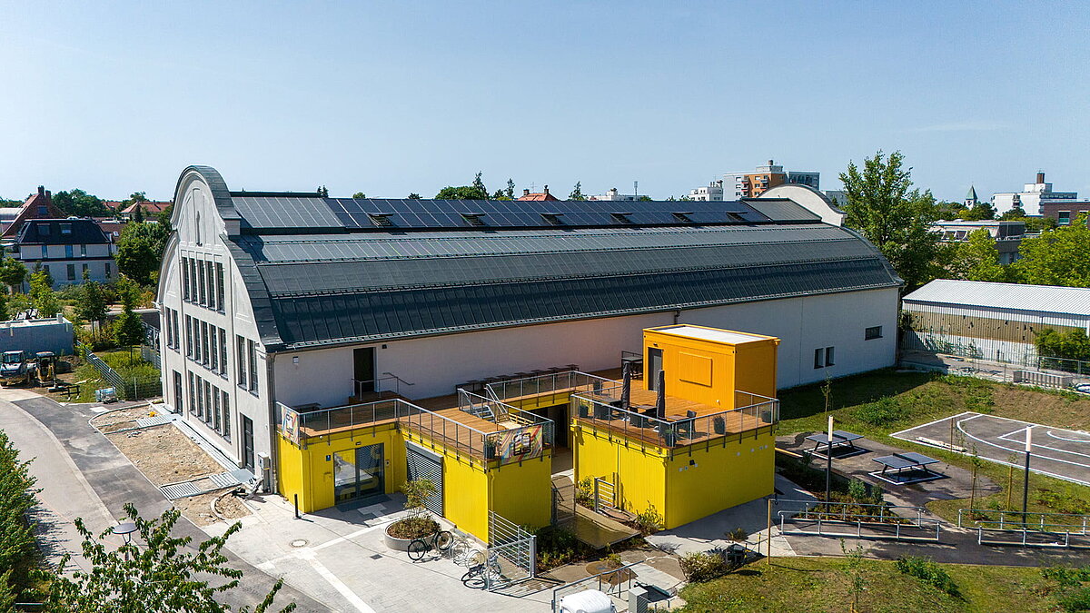 Modernisiertes Industriegebäude mit LAMILUX Glasdach und Photovoltaik, gelbe Anbauten im Vordergrund.