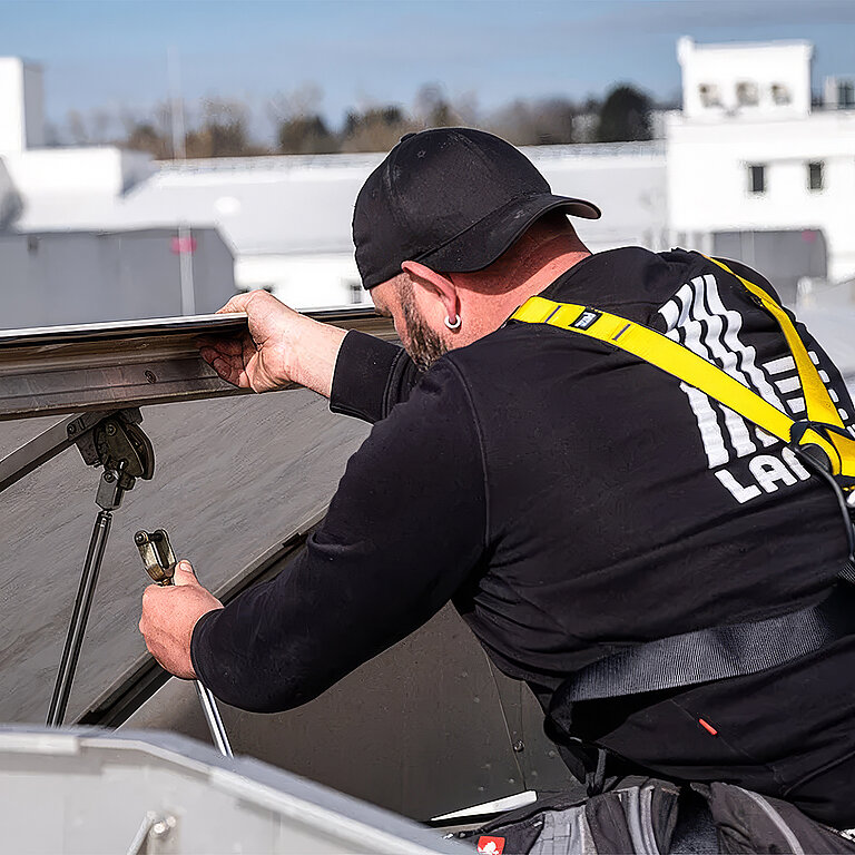 Dachdecker mit LAMILUX Shirt und Sicherheitsgurt bei der Montage einer Lichtkuppel