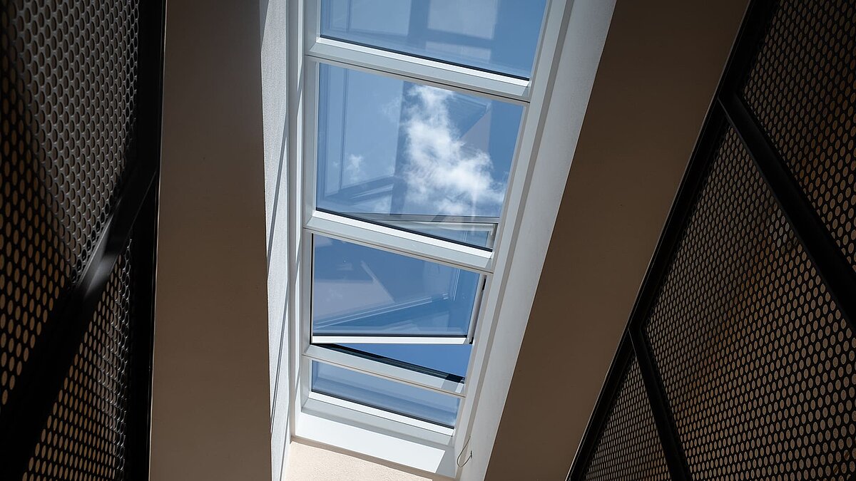 Blick durch ein modulares Glasdach von LAMILUX in einem Wohnhaus in Freiburg, mit Spiegelung des Himmels und Wolken.