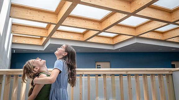Zwei Mädchen stehen auf einem Holzbalkon und blicken zur Decke
