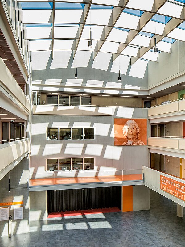 Innenansicht des Willibald-Gluck-Gymnasiums in Neumarkt mit großem Glasdach von LAMILUX, das den Raum mit Tageslicht durchflutet.