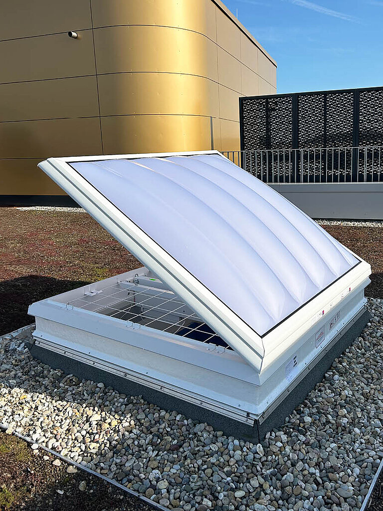 Geöffnete LAMILUX Lichtkuppel RWA auf Kies-Flachdach mit mehrschaliger Verglasung und weißem Aufsatzrahmen