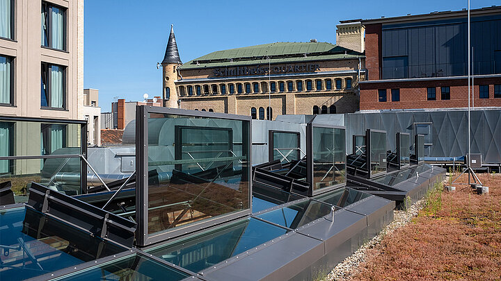 Geöffnete Glasdachfenster auf einem begrünten Flachdach mit Blick auf das historische Schultheiss-Quartier in Berlin