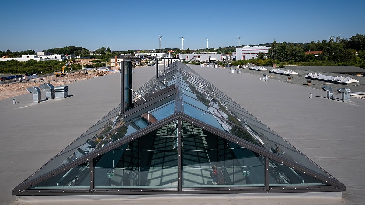 Großes Glasdach auf dem Flachdach des Outlet Center Selb, mit umliegendem Industriegebiet und Windrädern im Hintergrund.