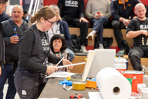 LAMILUX Mission Flachdach Teilnehmerin beim Ausmessen einer GFK Ecke auf Fachmesse"