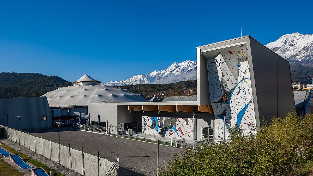 Moderne Kletterhalle mit bunter Boulderwand und schneebedeckten Bergen im Hintergrund