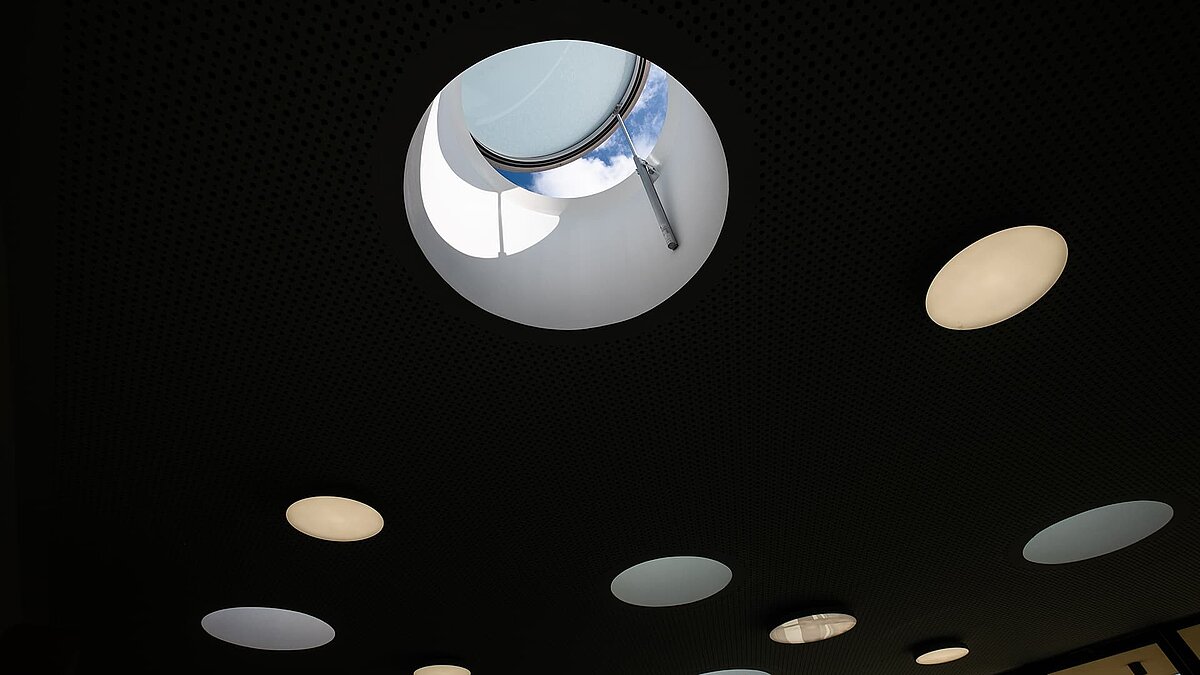Decke der Kindertagesstätte Sonnenfeld in Wandlitz mit runden Oberlichtern, eins davon geöffnet mit Blick auf den Himmel.