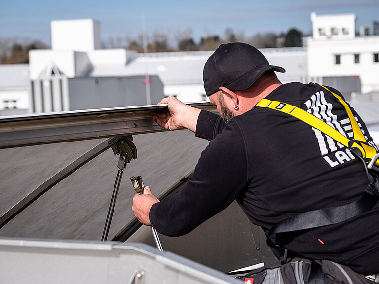 Handwerker arbeitet gesichert auf einem Flachdach und montiert ein Dachelement