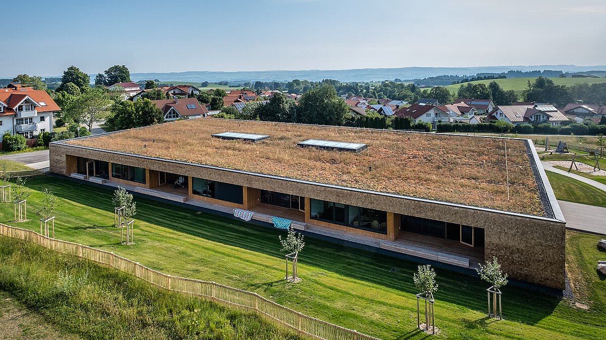 Kinderkrippe Wiggensbach mit begrüntem Flachdach und großflächigen Glasdächern für natürliches Licht.