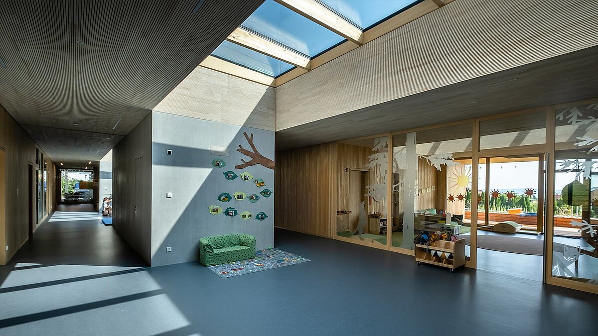 Innenraum der Kinderkrippe Wiggensbach mit großflächigen Glasdächern, die Tageslicht in den modernen, lichtdurchfluteten Raum bringen.