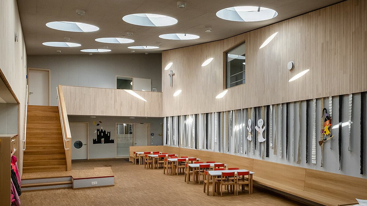 Innenraum des Kindergartens St. Severin mit runden Flachdachfenstern, die natürliches Licht in den Raum bringen.