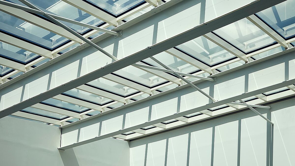 Detailaufnahme eines Glasdachs in Milton Park, England, mit weißen Stahlträgern und Sonnenlicht, das Schatten auf die Wände wirft.