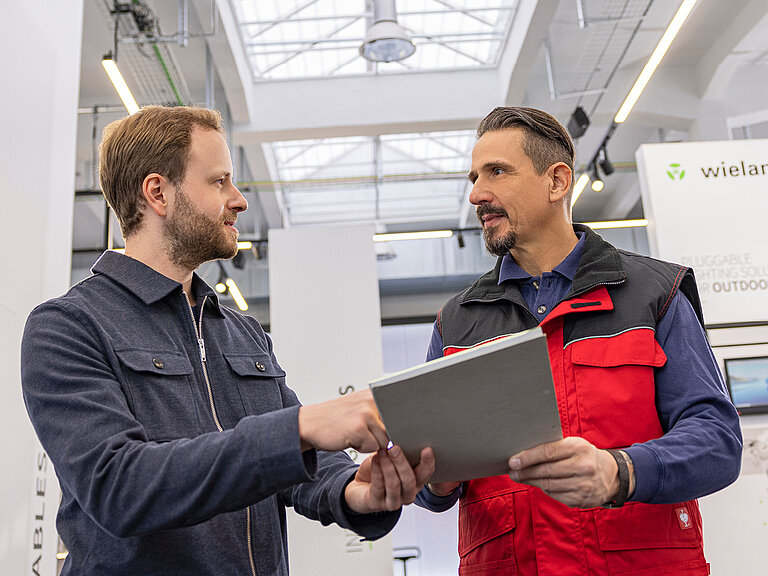 Zwei Männer besprechen ein Tablet in einer Industriehalle
