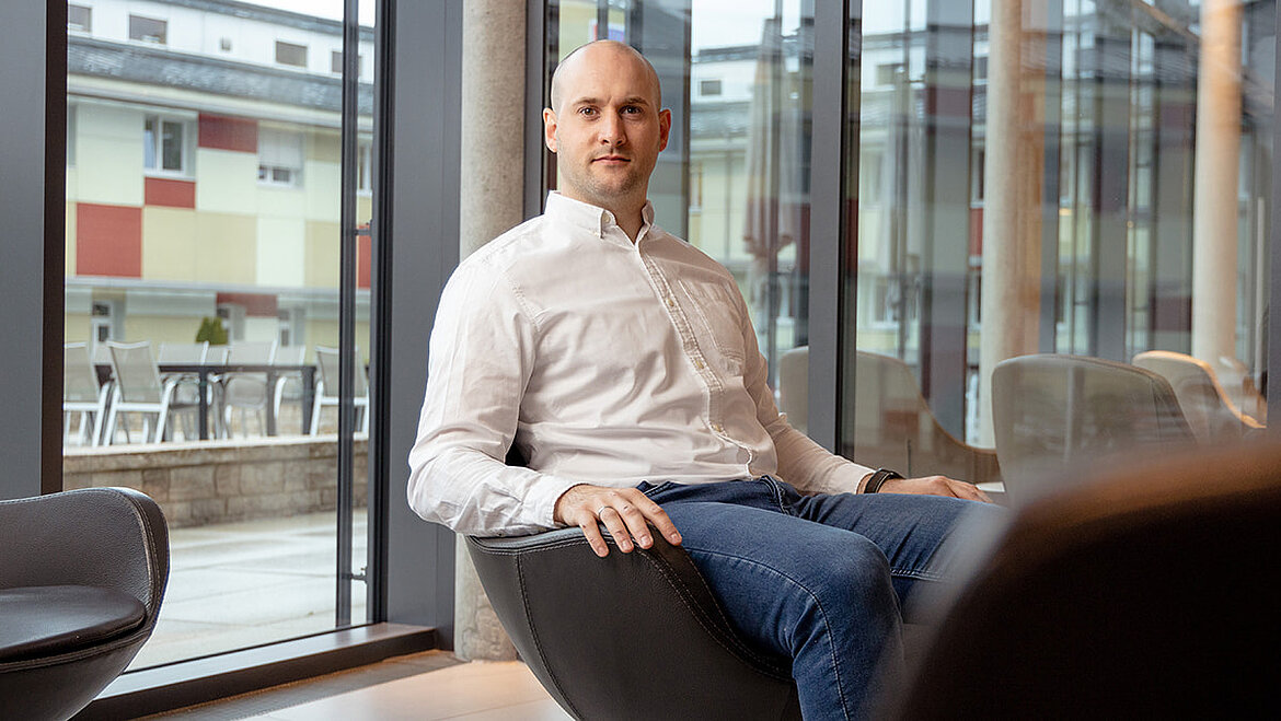 Mann sitzt in modernem Innenraum mit großen Glasflächen und Tageslicht