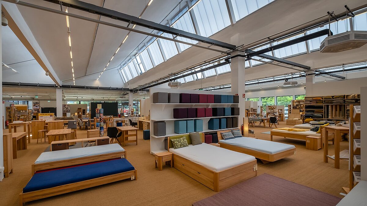 Innenansicht des alten Postbahnhofs Leipzig, mit Tageslicht durch große Lichtbänder und moderner Präsentation von Betten und Regalen.