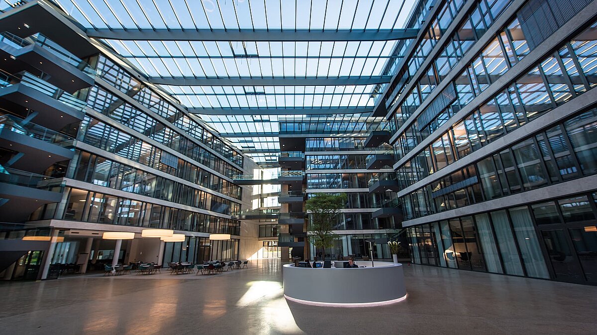 Großes, modernes Atrium des FGS Campus mit Glasdach, lichtdurchfluteten Bereichen, zentraler Rezeption und umliegenden Büroetagen.
