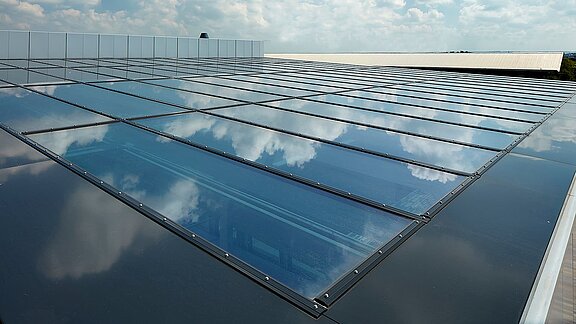 Glasdach der Gewerbeimmobilie im Milton Park, England, mit reflektierendem Himmel und Wolken auf der Oberfläche.