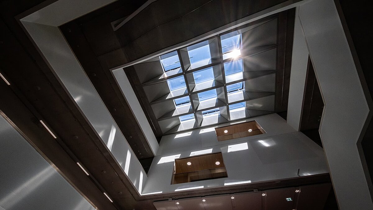 Innenaufnahme eines modernen Atriums mit Glasdach, Holzbalken und Sichtbetonwänden