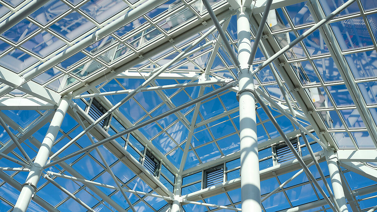Detailaufnahme der Stahlkonstruktion eines Glasdachs mit Gitterrahmen und blauem Himmel im Hintergrund