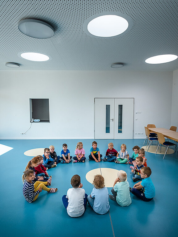 Gruppe von Kindern sitzt im Kreis in einem hellen Raum mit runden Oberlichtern