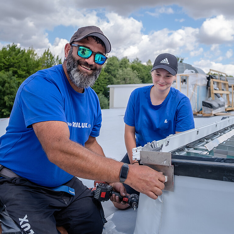 Zwei Handwerker montieren ein Tageslichtelement auf dem Flachdach