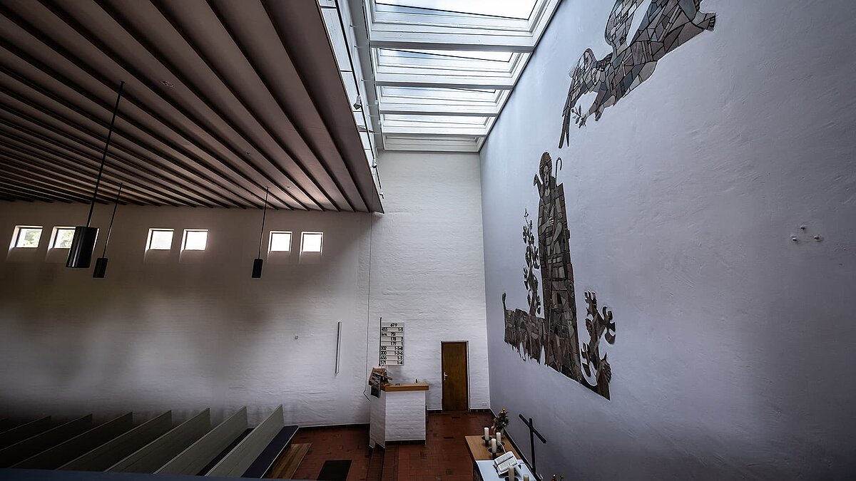 Innenraum der Pauluskirche in Traunreut mit LAMILUX Flachdachfenstern FE und einer großen Wandmosaik-Darstellung.