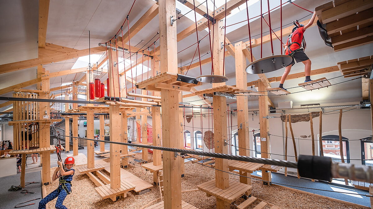 Indoor-Kletterpark mit Holzkonstruktion, Seilelementen und gesicherten Teilnehmern.