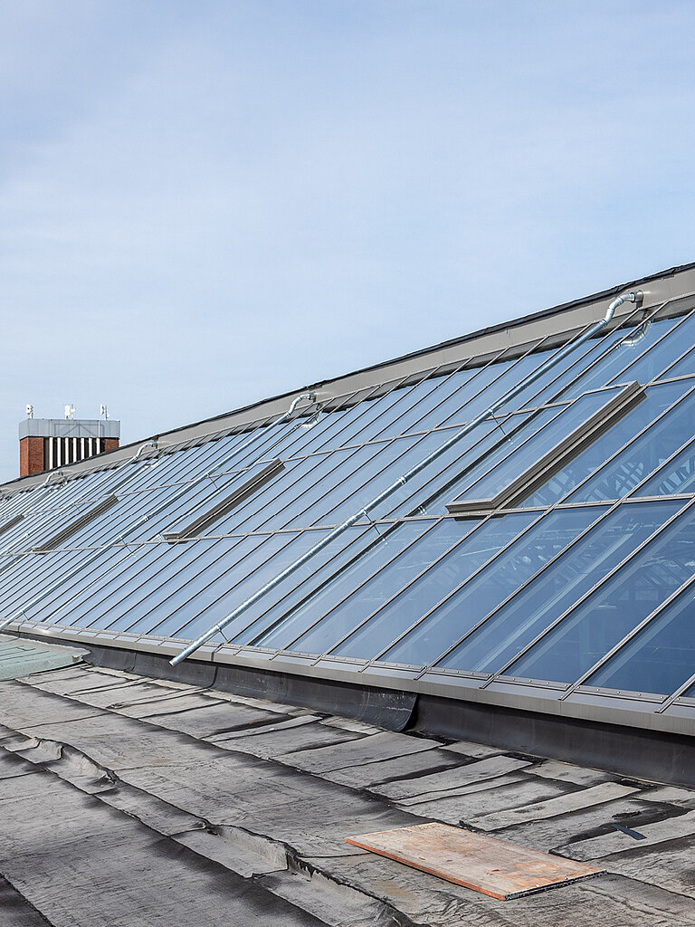 Geneigtes Dach mit großflächiger Glasdachkonstruktion und regelmäßig angeordneten Glasfeldern zur natürlichen Tageslichtnutzung