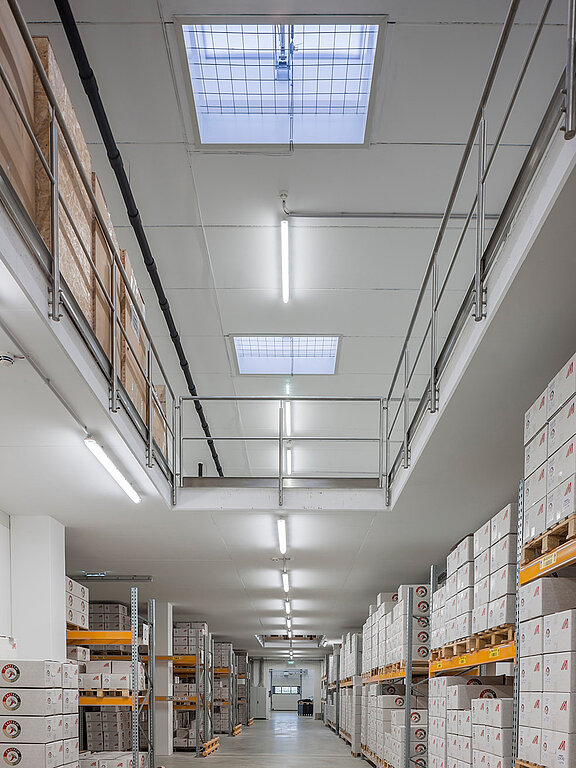 Lagerhalle mit Regalen voller Kisten und Oberlichtern in der Decke.