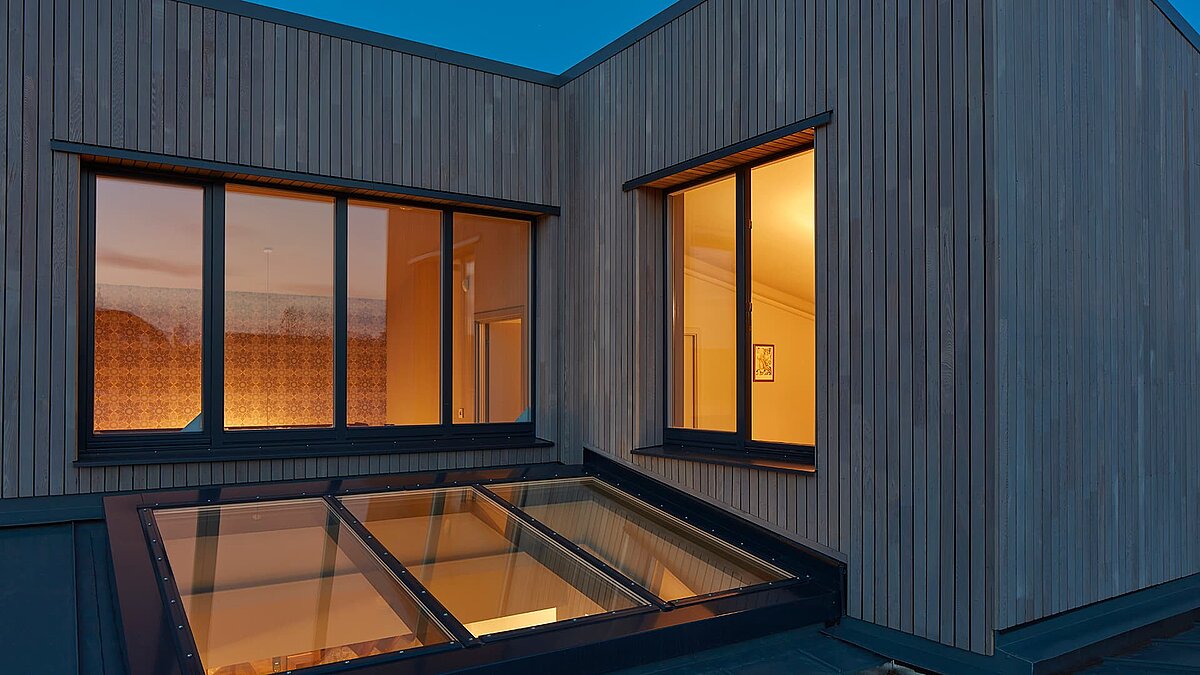 Außenansicht der Potton Show Homes in England bei Dämmerung mit LAMILUX Glasdach PR60 und beleuchtetem Innenraum.