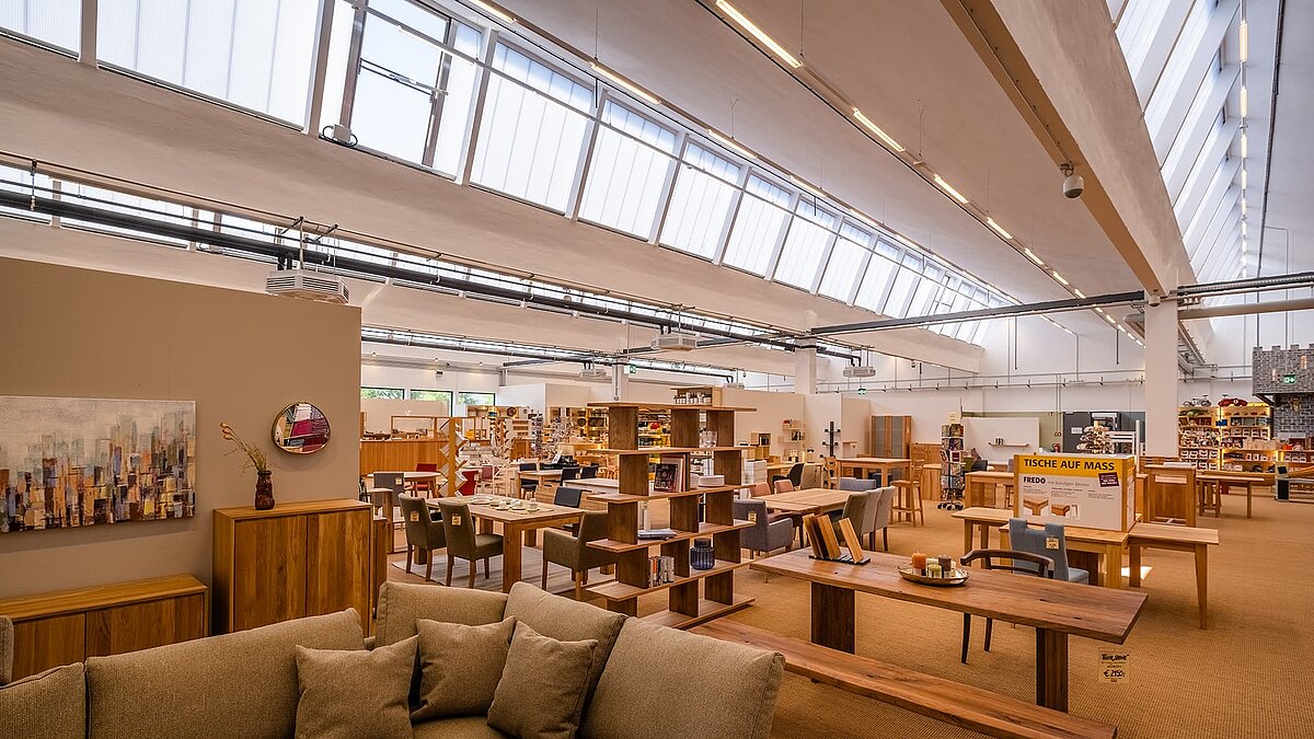 Innenansicht des alten Postbahnhofs Leipzig, umgestaltet als Möbelgeschäft mit modernem Design, natürlichen Lichtbändern und stilvollen Möbeln.