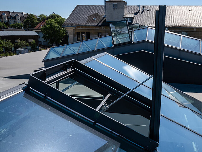 Mehrere verglaste Dachoberlichter auf geneigtem Metalldach, Ansicht von oben mit sichtbarer Rahmenkonstruktion und umliegender Bebauung
