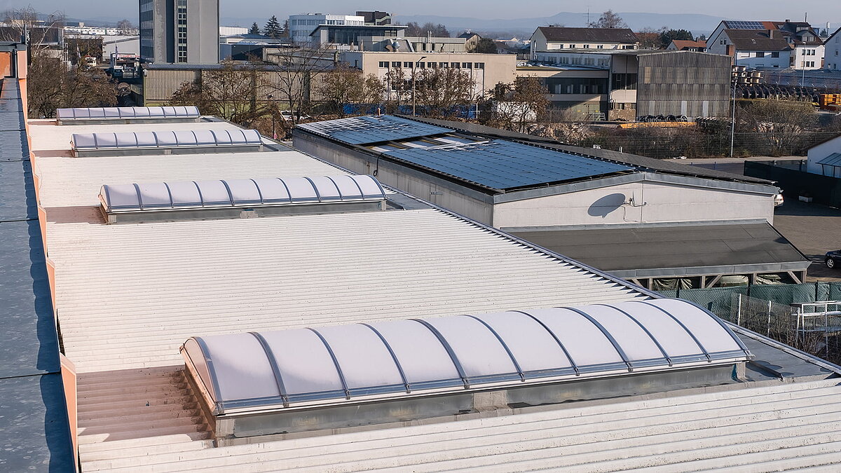 Dach des OBI Baumarkts in Bamberg mit gebogenen Lichtbändern zur natürlichen Beleuchtung, umgeben von Industriegebäuden und Solaranlagen.