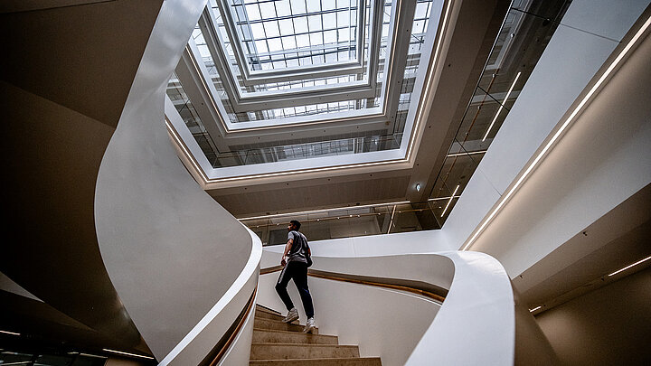 Person geht eine moderne Wendeltreppe in einem lichtdurchfluteten Atrium hinauf.