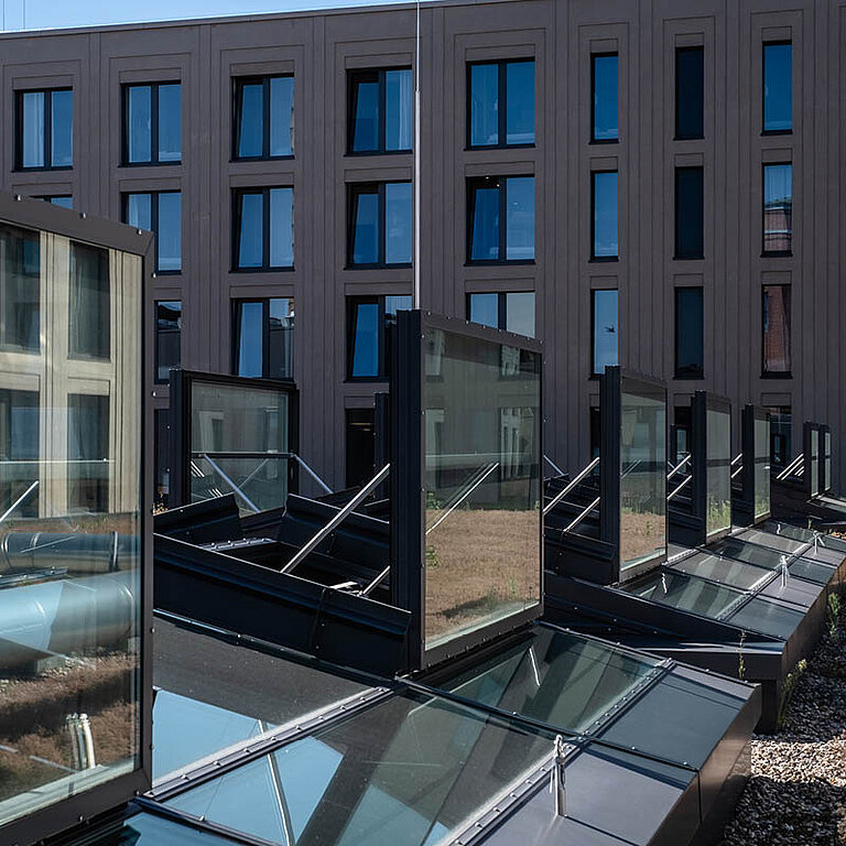 Mehrere geöffnete LAMILUX Glasdach RWA in einem Innenhof mit Glasbrüstungen und umliegender Gebäudefassade