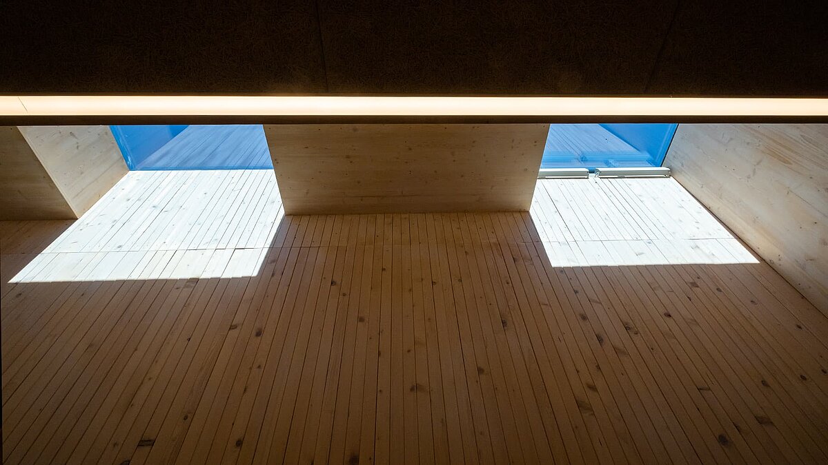 Innenraum der Kinderkrippe Waltenhofen mit natürlichem Tageslicht durch Dachfenster, Holzwände und Schattenwurf.
