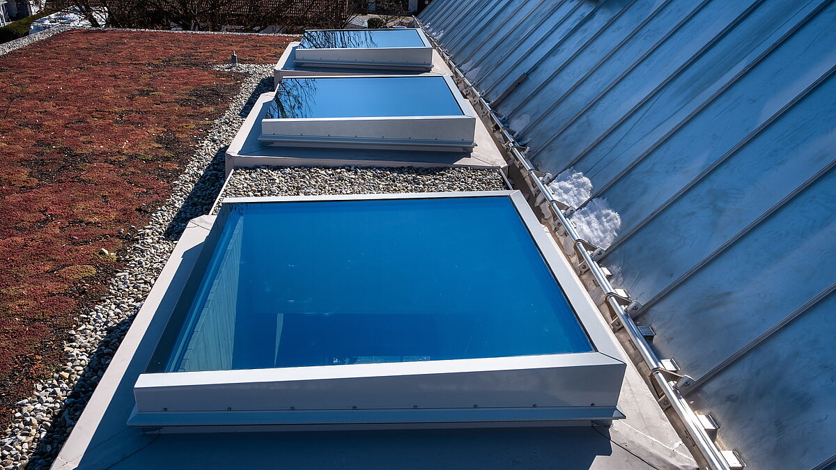 Flachdach mit großen Oberlichtern der Kinderkrippe Waltenhofen und begrüntem Dachbereich.