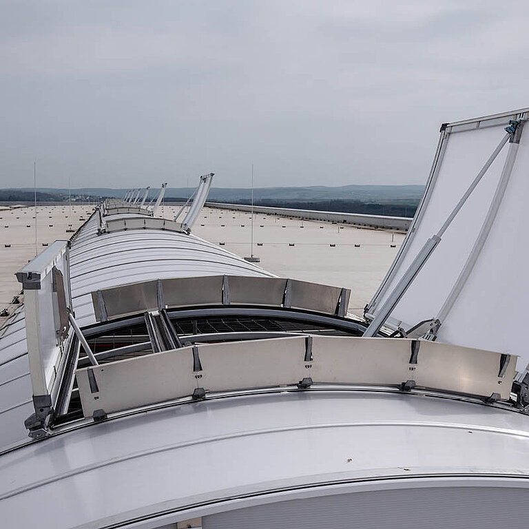 Geöffnetes LAMILUX Lichtband B RWA auf Industrie-Flachdach mit bogenförmiger Verglasung
